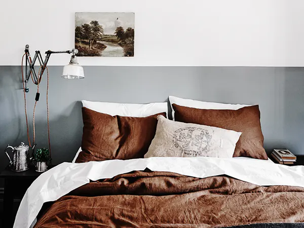 Image of bed with lamp and painting of countryside.