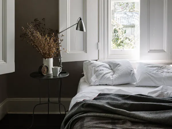 Image of bed with bedside table, and window facing out to a backyard.